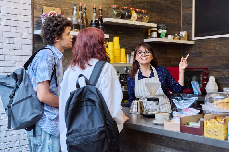 Zwei Kunden sprechen mit einer Frau im Café, es sieht nach Small Talk aus