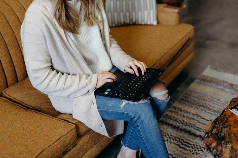 Frau sitzt auf einem Sofa und bucht einen Termin online auf ihrem Laptop