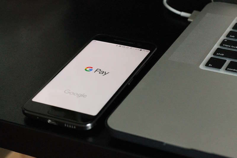 Google Pay auf einem Smartphone neben einem Laptop