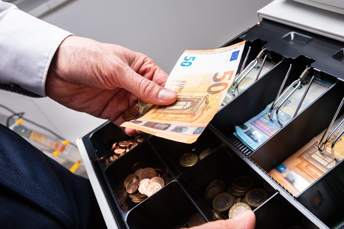 Person sortiert 50 Euro in eine Kassenschublade ein