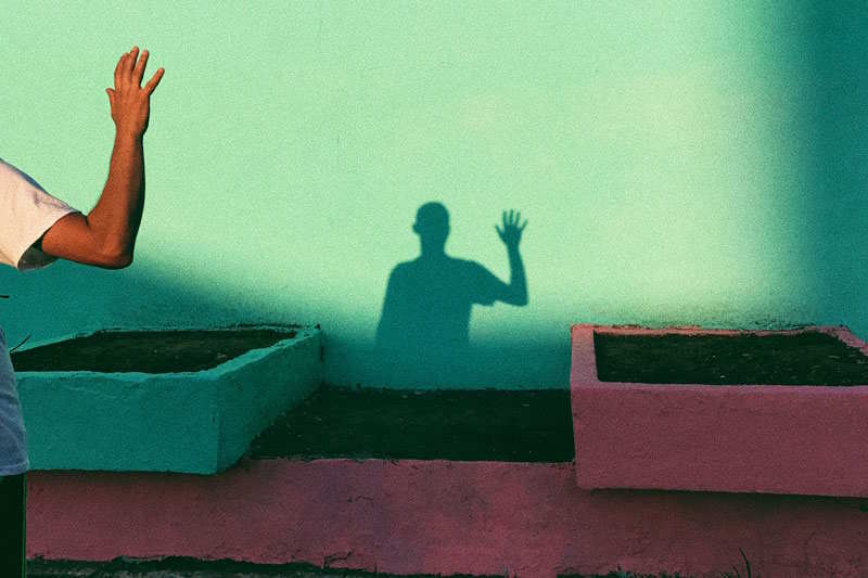Eine Person und ihr Schatten winken sich an einer grünen Wand zu