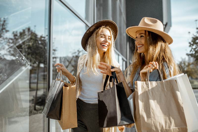 Zwei glückliche Freundinnen schauen auf das Schaufenster, während sie mit Einkaufstüten in der Nähe des Einkaufszentrums stehen